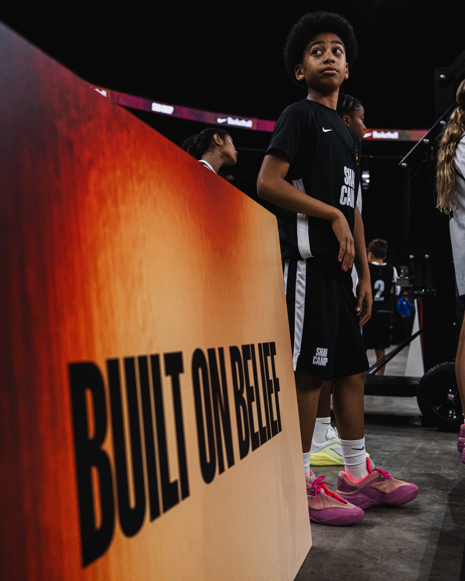 A young athlete standing beside a Built on Belief sign at SGA Camp